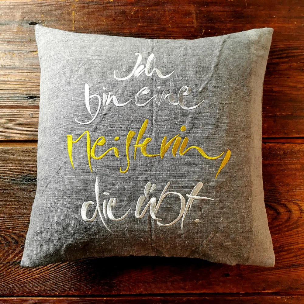 Graue Kissenhülle „Ich bin eine Meisterin, die übt.“ aus handgewebtem Vintage-Bauernleinen, 40x40 cm, als edles Deko-Unikat auf einem Sofa arrangiert