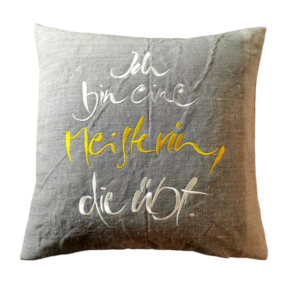 Graue Kissenhülle „Ich bin eine Meisterin, die übt.“ aus handgewebtem Vintage-Bauernleinen, 40x40 cm, als edles Deko-Unikat auf einem Sofa arrangiert
