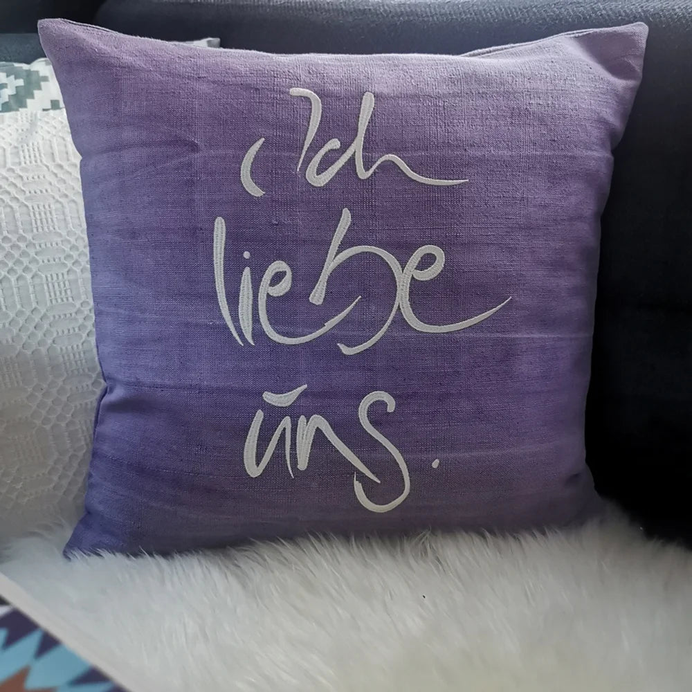 Hellviolette Kissenhülle „Ich liebe uns“ aus handgewebtem Vintage-Bauernleinen, 40x40 cm, dekoriert auf einem Sofa als romantisches Deko-Unikat