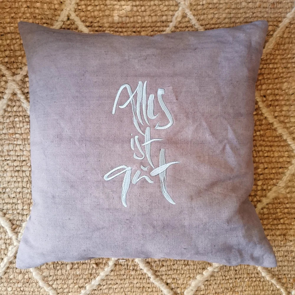 grauen Vintage-Bauernleinen-Kissenhüllen, oben das Unikat mit hellblauer „Alles ist gut“-Stickerei, symbolisiert exklusive, handgefertigte Deko