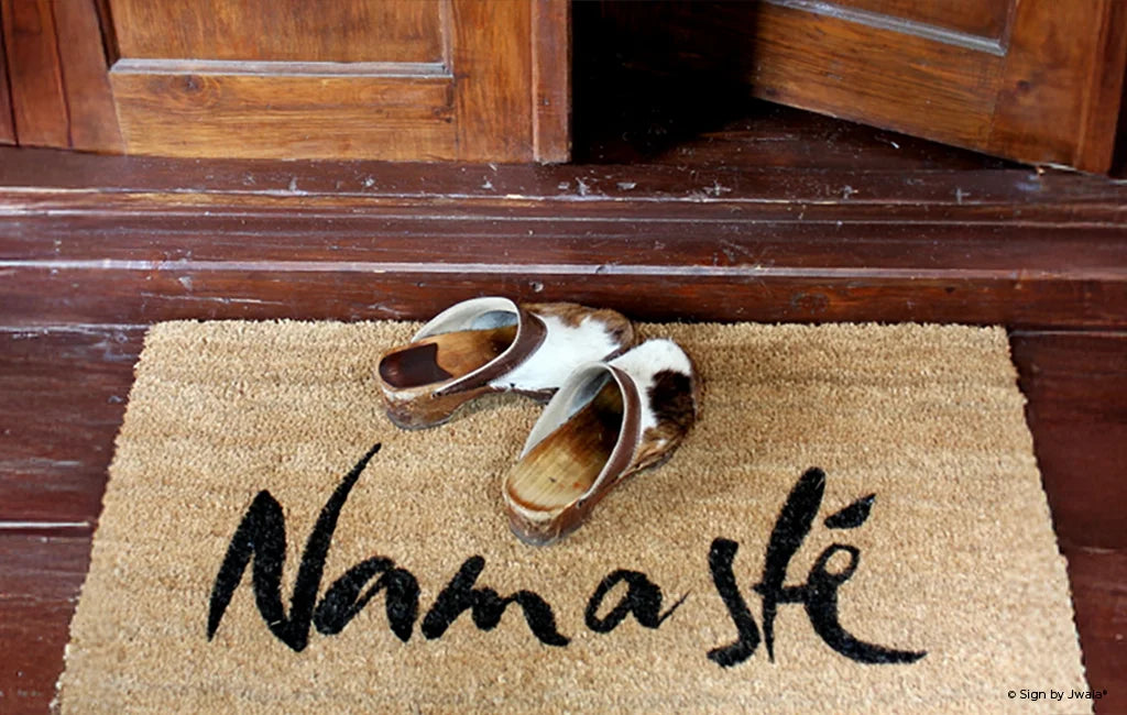 Das Bild zeigt eine Fußmatte aus dem Onlineshop SignShop Tirol, die vor einer Holztür liegt. Darauf stehen traditionelle Holzschuhe – die Szene wirkt einladend, warm und vermittelt ein Gefühl von Zuhause.