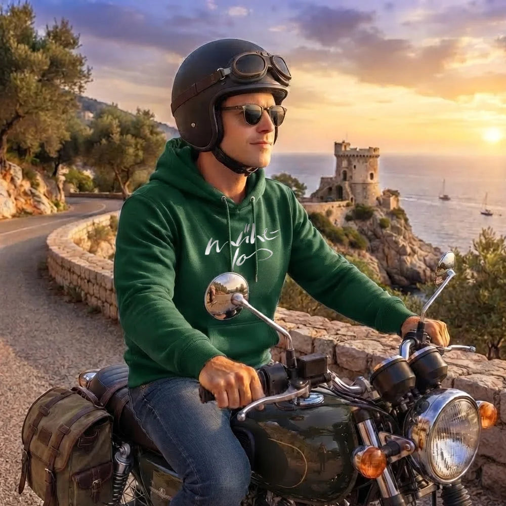 Motorradfahrer auf einer Panorama-Küstenstraße im dunkelgrünen Kapuzenpullover mit dem geschwungenen, weißen Schriftzug-Sign „In love to“.