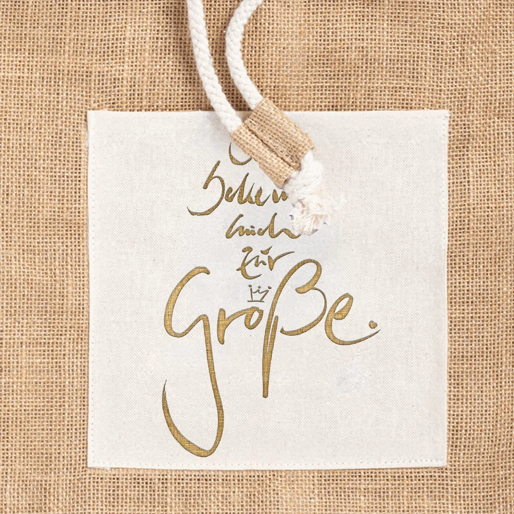 Nahaufnahme der weißen Baumwolltasche auf dem Jute-Seesack mit dem goldenen Sign Ich bekenne mich zur Größe