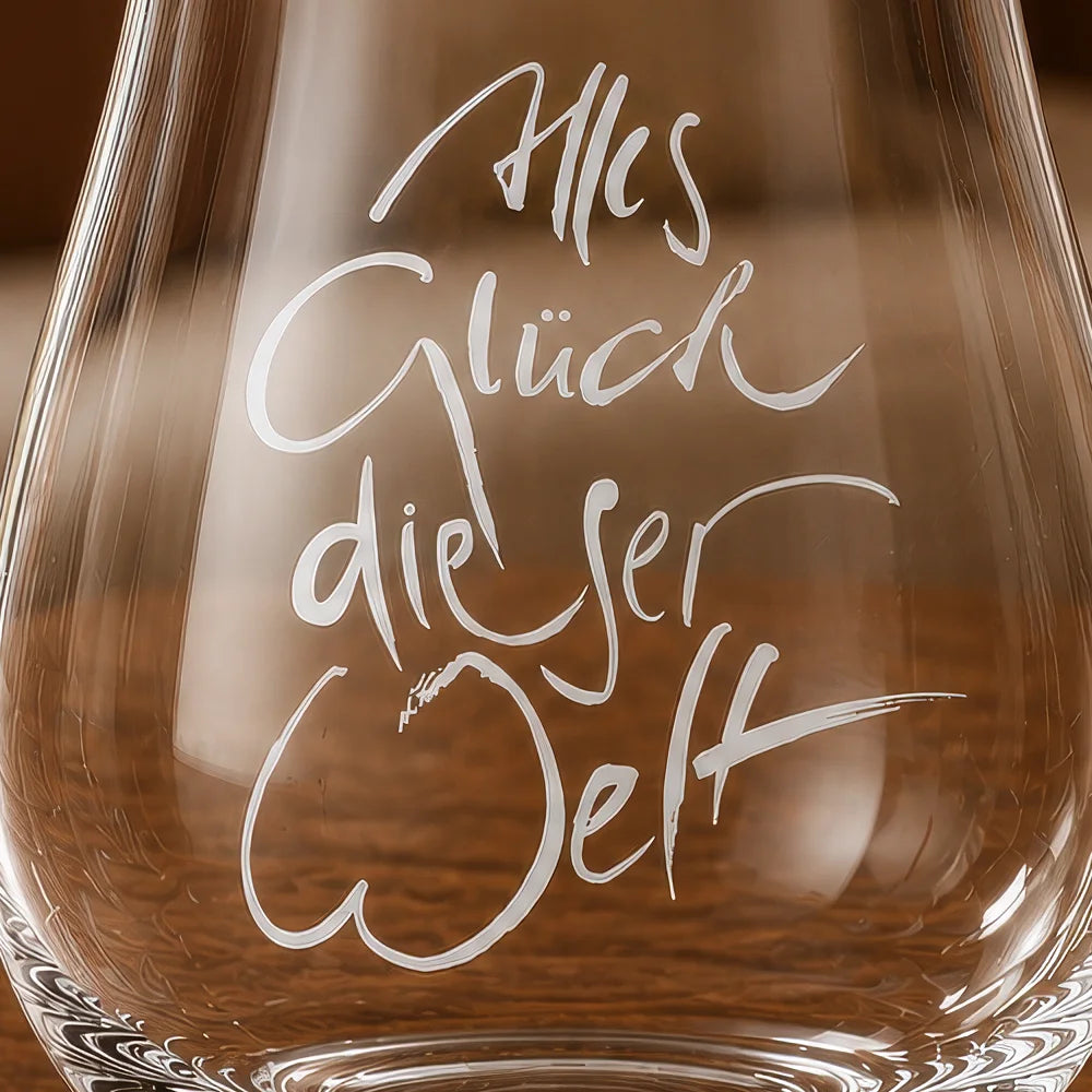 Detailaufnahme der eleganten, handschriftlichen Gravur „Alles Glück dieser Welt“ auf dem hochwertigen Tiroler Kristallglas von Riedel.