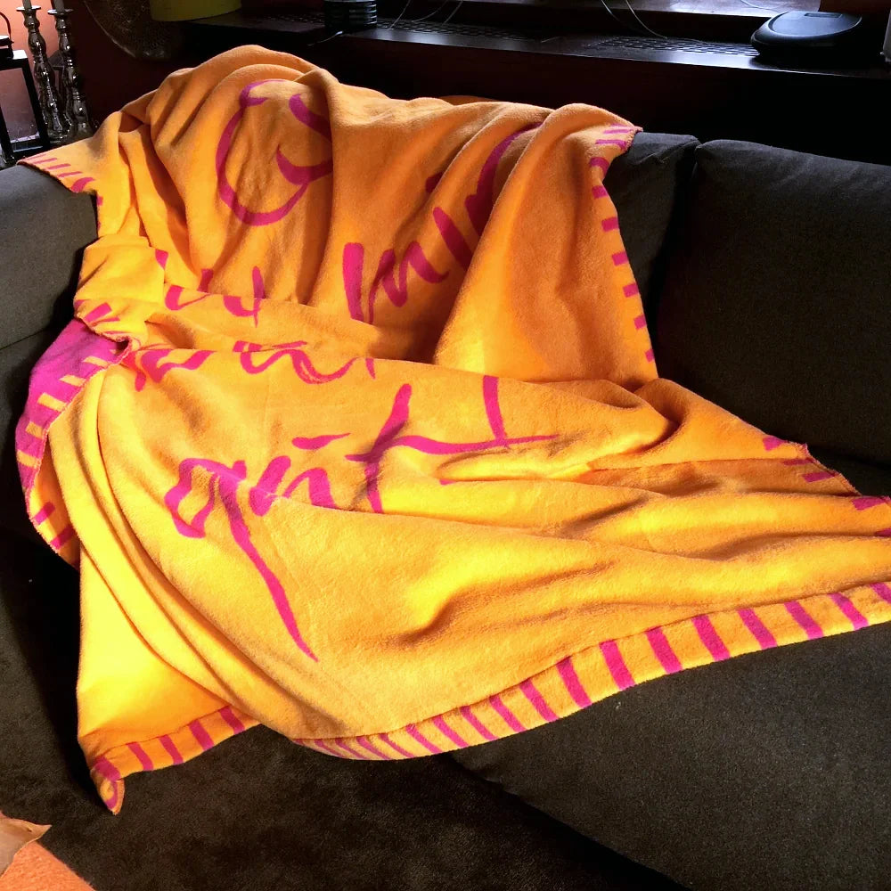Gemütliche Kuscheldecke mit inspirierender Botschaft drapiert über einer dunklen Stele oder einem Steinblock im Garten.