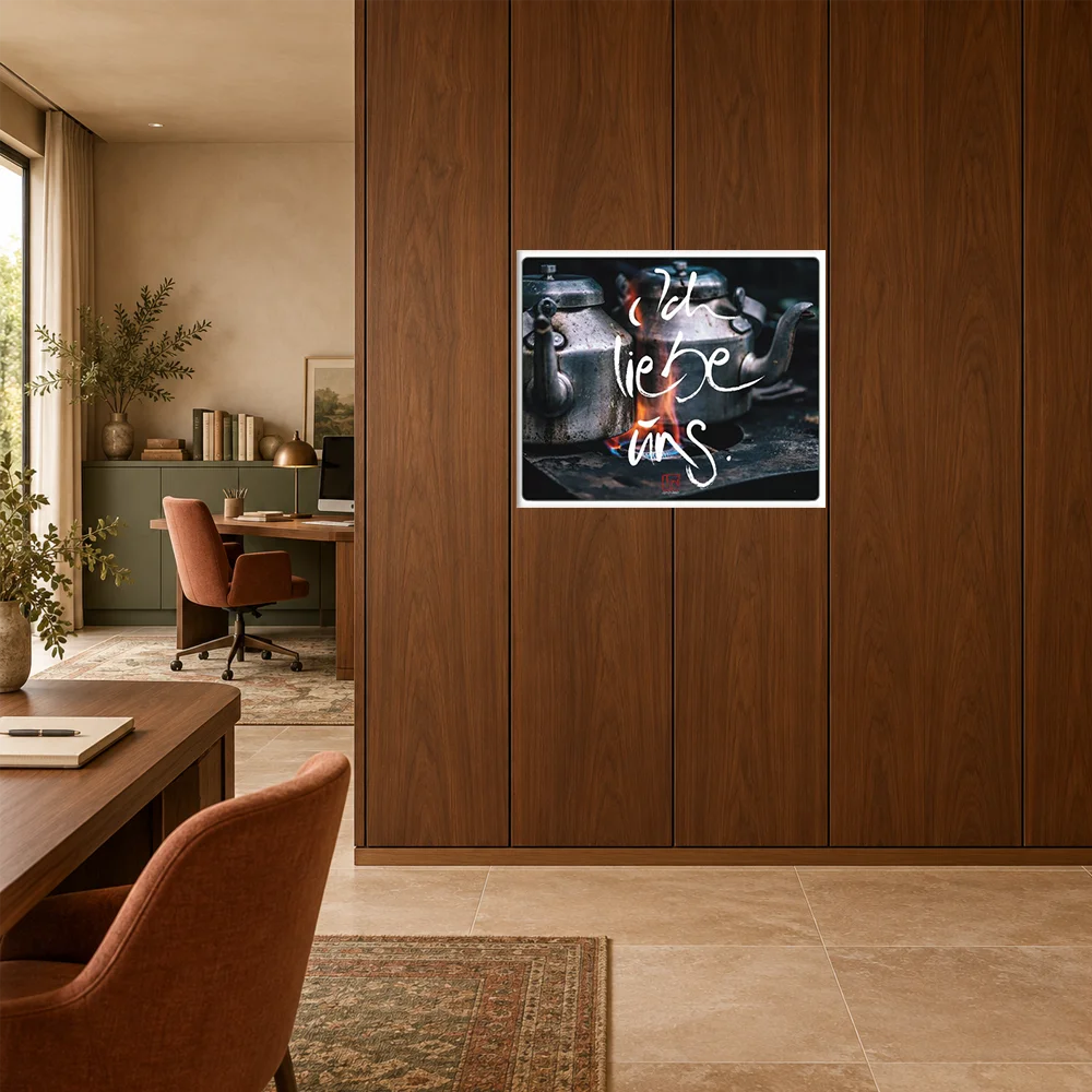 Fotokunst-Poster auf Alu-Dibond "gebürstet" mit zwei traditionellen Teekesseln auf einem Herd und dem Text Sign by Jwala „Ich liebe uns“, aufgehängt an einer dunklen Furnierwand im Arbeitsbereich.