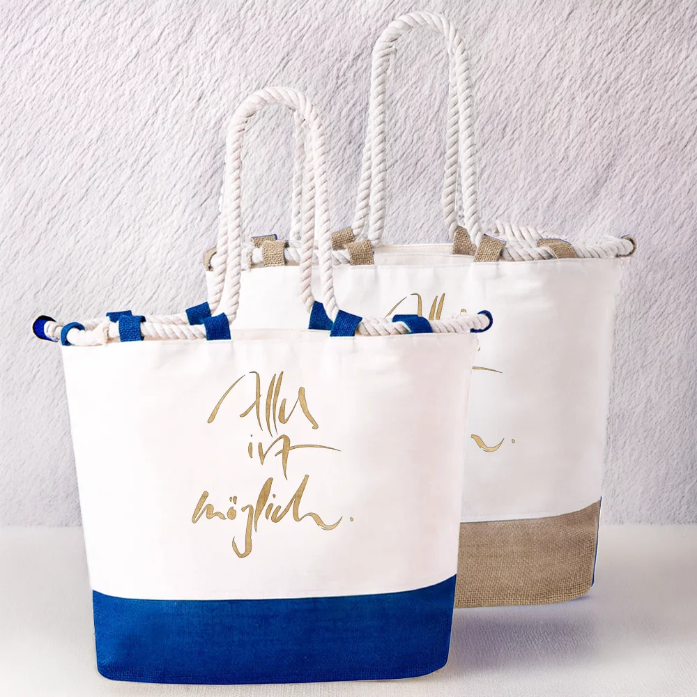 Zwei veredelte Strandtaschen im Set. Im Vordergrund steht die Variante mit blauem Juteboden und der goldenen Aufschrift „Alles ist möglich.“, dahinter die Variante mit naturfarbenem Juteboden und der Aufschrift „Ich bin so frei“.