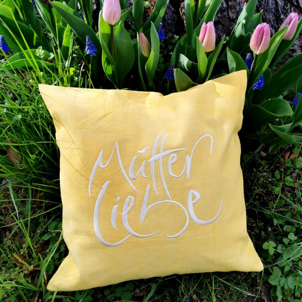 Dekokissen-Arrangement im Blumenbeet mit Kissenhülle „Mutterliebe“ aus Tirol