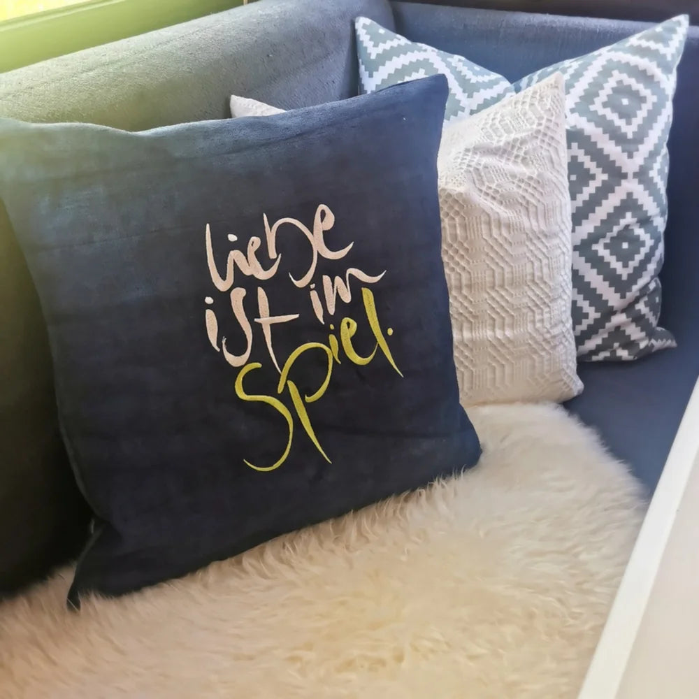 Detailaufnahme der creme-hellgrünen Stickerei „Liebe ist im Spiel“ (Sign by Jwala®) auf dunkelblauer Bauernleinen-Kissenhülle