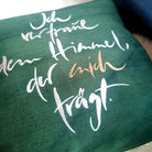 Detailaufnahme der mehrfarbigen Stickerei „Ich vertraue dem Himmel, der mich trägt“ (Sign by Jwala®) auf dunkelgrüner Bauernleinen-Kissenhülle