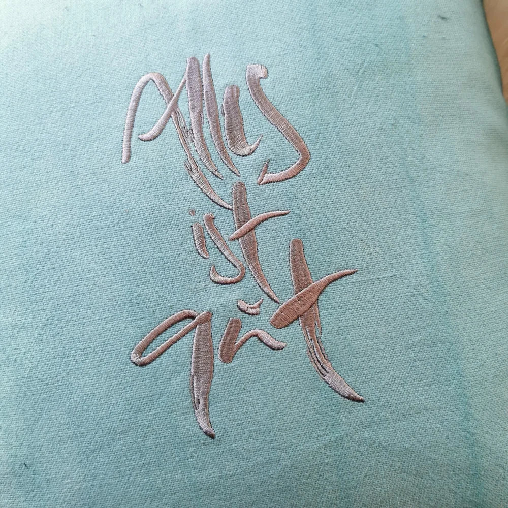 Detailaufnahme der grauen Stickerei „Alles ist gut“ (Sign by Jwala®) auf mintfarbener Bauernleinen-Kissenhülle mit sichtbarer Leinenstruktur