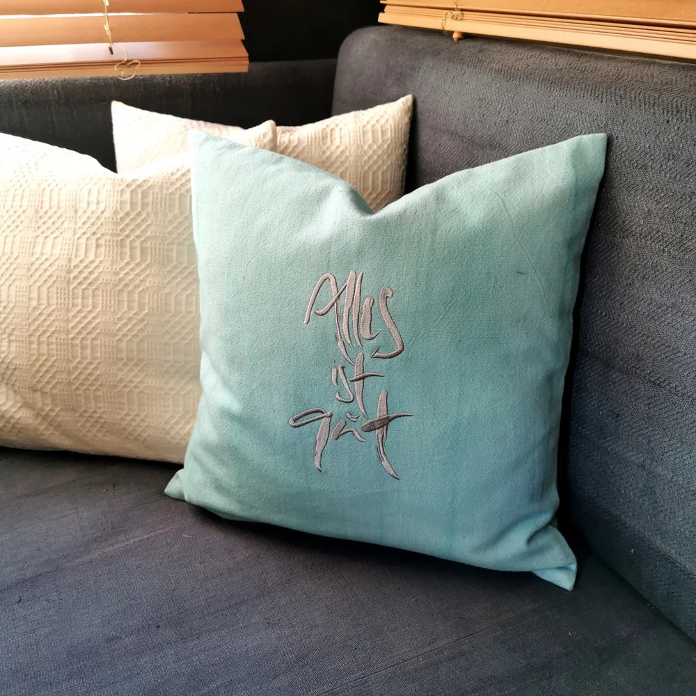 Mintfarbene Kissenhülle „Alles ist gut“ aus handgewebtem Vintage-Bauernleinen, 40x40 cm, dekoriert auf einem hellen Sofa als edles Deko-Unikat