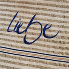 Detailansicht Tischläufer „Liebe“ – blaue Sign-Stickerei auf gestreiftem Bauernleinen