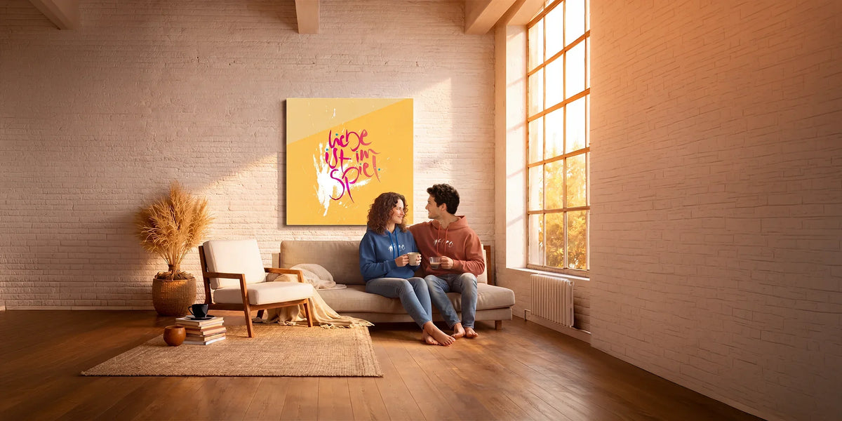 Modernes Interior Design im Boho-Stil mit einem farbenfrohen, gelben Typografie-Wandbild als Statement mit dem Sign "ILiebe ist im Spiel"über dem Sofa im Wohnzimmer.