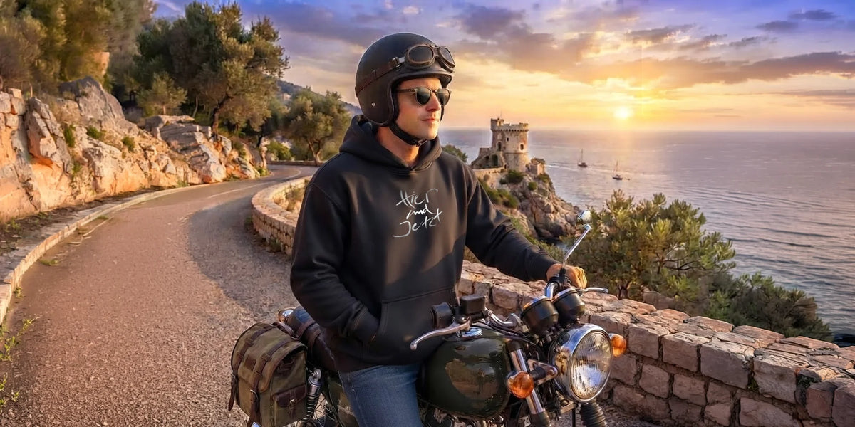 Ein Motorradfahrer genießt die Abenddämmerung an einer Panoramastraße am Meer, bekleidet mit einem modernen Oversized-Hoodie von Sign Shop Tirol.