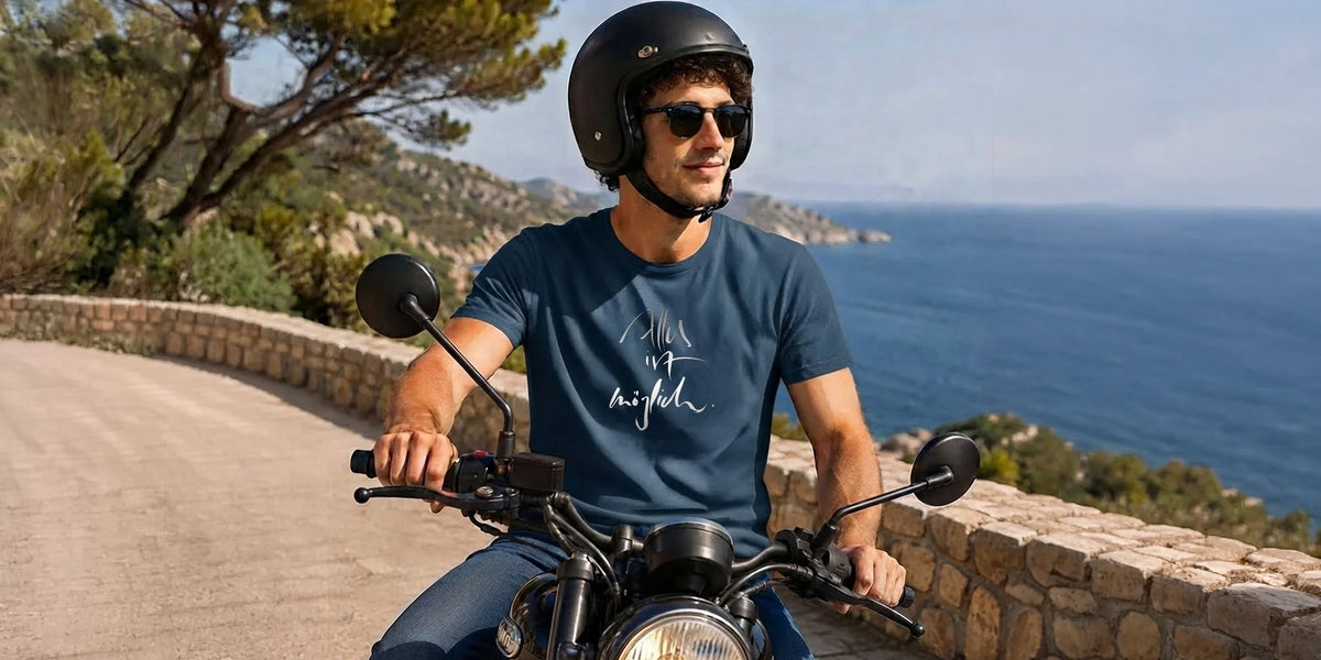 Dynamische Nahaufnahme eines Bikers auf einem Custom-Motorrad, der ein dunkelblaues Baumwoll-T-Shirt mit weißem Motivaufdruck von Sign by Jwala trägt.