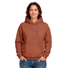 Frau im oversized Kapuzenpullover in Heritage Brown mit einem mehrzeiligen, feinen Sign "Gehen wohin das Leben will" auf der Vorderseite.