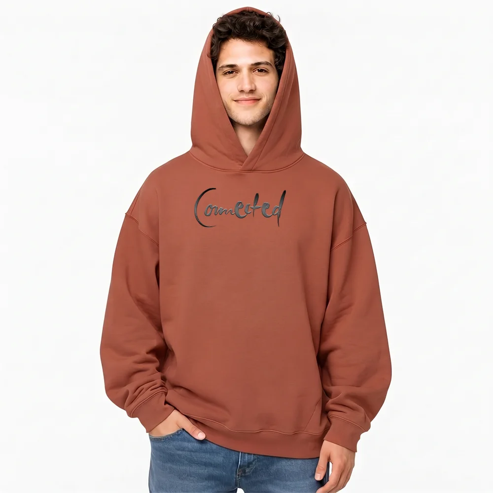 Vorderansicht eines Mannes im terracottafarbenen Kapuzenpullover mit aufgesetzter Kapuze und dem dunklen Sign „Connected“ auf der Brust.