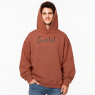 Vorderansicht eines Mannes im terracottafarbenen Kapuzenpullover mit aufgesetzter Kapuze und dem dunklen Sign „Connected“ auf der Brust.