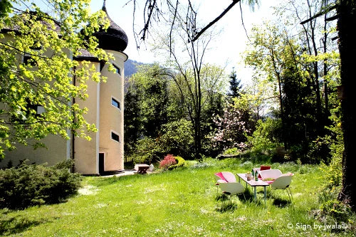 Claudiaschlössl umgeben von Wiese und Wald, im Vordergrund ein einladender Tisch mit Stühlen – ein Ort in Kramsach, Tirol, voller Natur, Ruhe und Herzenswärme.