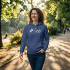 Lächelnde Frau mit lockigem Haar geht im Park spazieren und trägt einen blauen Damen-Kapuzenpullover mit weißem Sign #Goo vom Signshop Tirol.