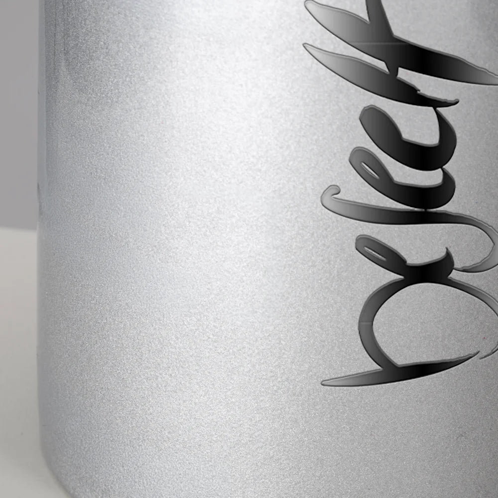 Nahaufnahme der glitzernden, silbernen Oberfläche einer Keramiktasse mit dem spiegelnden schwarzen Aufdruck Sign by Jwala® "beseelt".