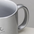 Makroaufnahme des ergonomischen Henkels und des oberen Randes einer silbernen Metallic-Kaffeetasse mit weißem Innenleben und Sign by Jwala®.