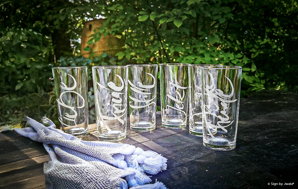 Wassergläser mit inspirierender Botschaft auf einem Holztisch im Garten aus dem Onlineshop SignShop Tirol.