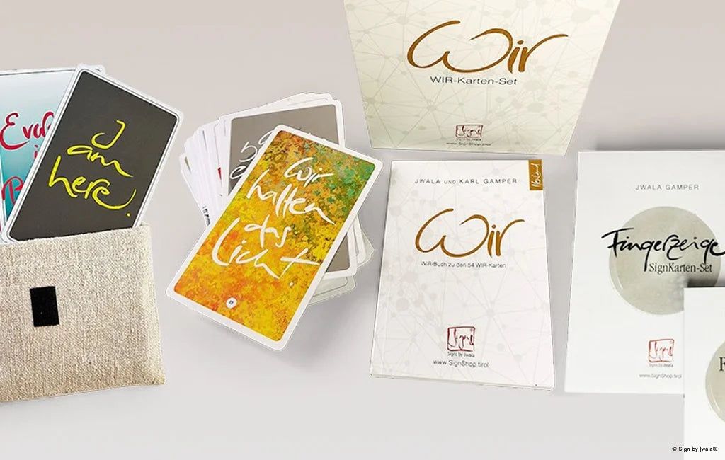 Orakelkarten von Signs by Jwala® im hochwertigen Bauernleinen-Beutel. Im Vordergrund liegt auch das Buch „Fingerzeige“, und das Buch von Jwala und Karl Gamper mit dem Titel "WIR". Die Szene vermittelt liebevolle Handarbeit, Natürlichkeit und eine einladende Atmosphäre voller Inspiration.