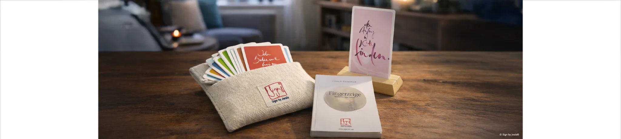 Inspirationskarten von Signs by Jwala®  im Bauernleinen-Beutel, vorne das Buch „Fingerzeige“ von Karl und Jwala Gamper dahinter ein Holzständer mit Orakelkarte.