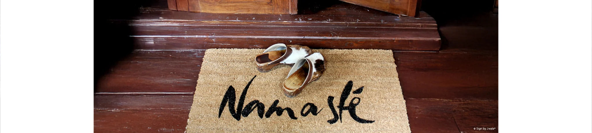 Das Bild zeigt eine Fußmatte aus dem Onlineshop SignShop Tirol, die vor einer Holztür liegt. Daneben stehen traditionelle Holzschuhe – die Szene wirkt einladend, warm und vermittelt ein Gefühl von Zuhause.