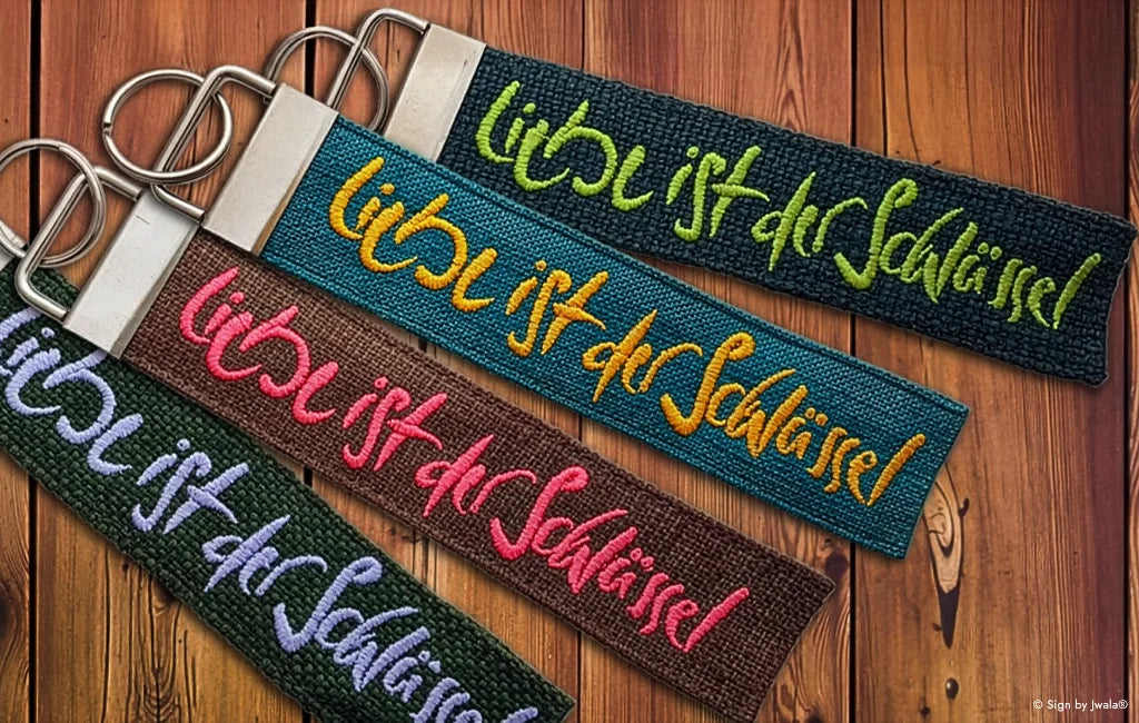 Verschiedene handgemachte Schlüsselanhänger und Taschenbaumler aus Bauernleinen mit der Botschaft „Liebe ist der Schlüssel“, liebevoll gefertigt und im Onlineshop SignShop Tirol erhältlich.