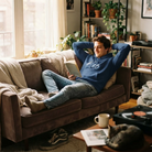 Entspannter Mann liest ein Buch auf dem Sofa und trägt einen blauen Herren-Hoodie mit stilvollem, weißem Sign - #600.