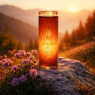 Veredelte SignKerze „Alles Glück dieser Welt“ im Glas – Leuchtende Kerze in Rot-Orange mit inspirierender Botschaft, fotografiert auf einem Felsen bei Sonnenuntergang über einem weiten Tal – exklusiv im SignShop Tirol erhältlich