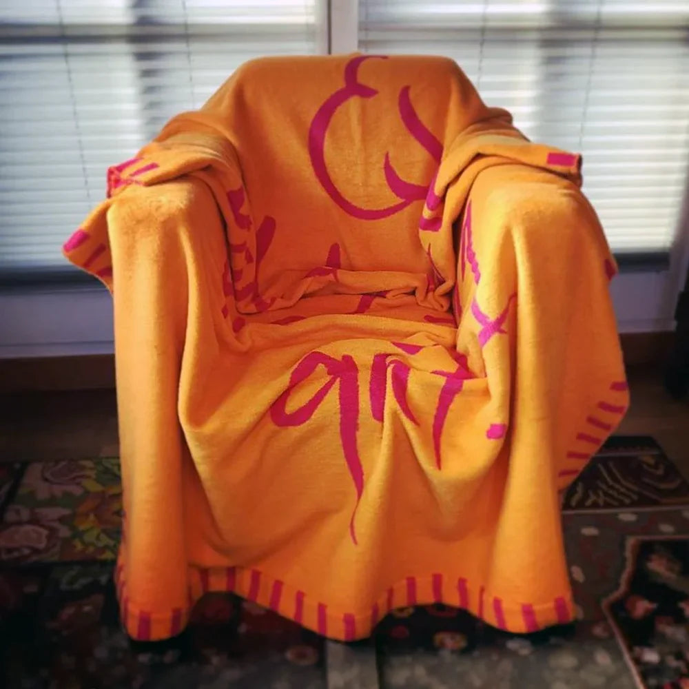 Orange-pinke Kuscheldecke komplett ausgebreitet über einem gemütlichen Sessel vor einem Fenster mit Jalousien.
