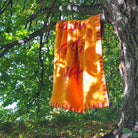 Die farbenfrohe Wohndecke in Orange und Fuchsia hängt dekorativ über einem Ast eines grünen Baumes in der Natur.