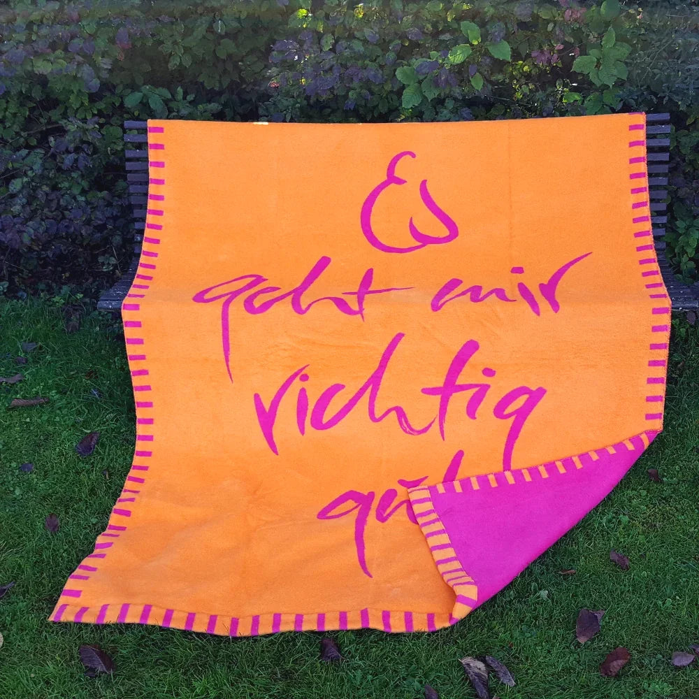 Detailansicht der Naturfaser-Kuscheldecke in Orange mit umgeschlagener Ecke, die die fuchsienrote Rückseite zeigt.
