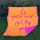 Detailansicht der Naturfaser-Kuscheldecke in Orange mit umgeschlagener Ecke, die die fuchsienrote Rückseite zeigt.
