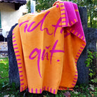 Kuscheldecke aus einer Vorarlberger Manufaktur in Orange und Fuchsia, angelehnt an einen Holzzaun im herbstlichen Garten.