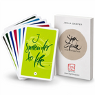 Das Begleitbuch „SignGuide“ aufrecht stehend neben einem Stapel der 54 SignCards, wobei die vorderste grüne Karte mit dem kalligrafierten Spruch „I surrender to life.“ zu sehen ist.