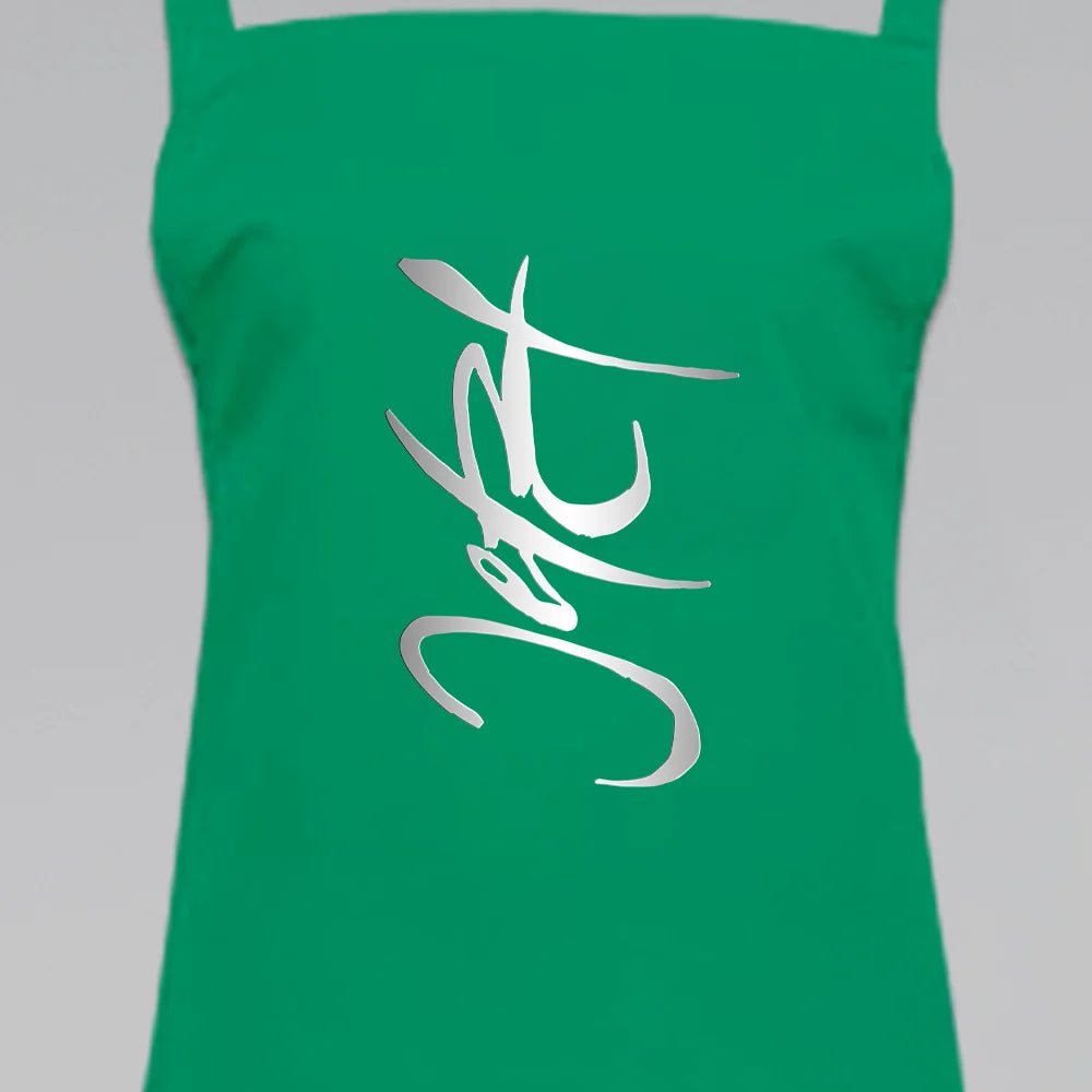 Grüne Latzschürze bedruckt mit dem silberfarbenen Jwala® Sign „Jetzt“ in moderner, dynamischer Kalligrafie-Schrift – gestaltet von SignShop.tirol.