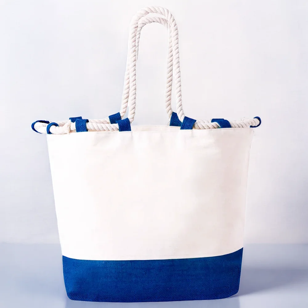 Schlichte, zweifarbige Strandtasche aus weißer Baumwolle mit einem breiten, tiefblauen Juteboden und dicken, hellen Seilgriffen ohne Aufdruck.